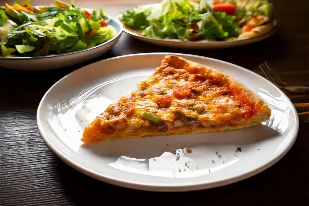 A slice of pickle pie pizza on a plate with a side salad.